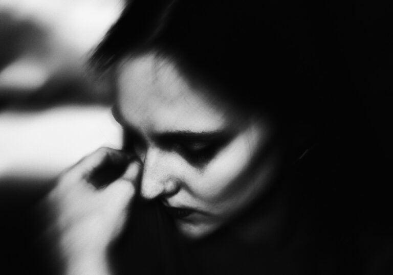 A woman has a hand on her should/by her face, her face is downturned, she looks sad.